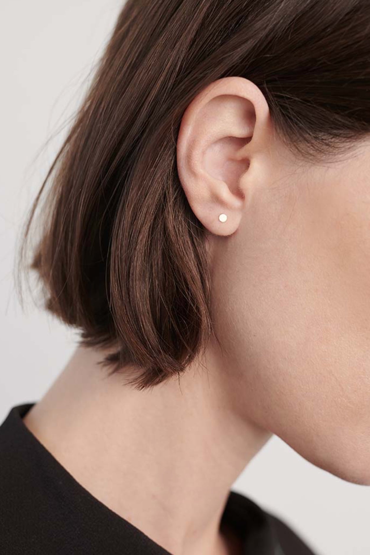 Model wearing small gold disc stud earrings with organic matte texture.