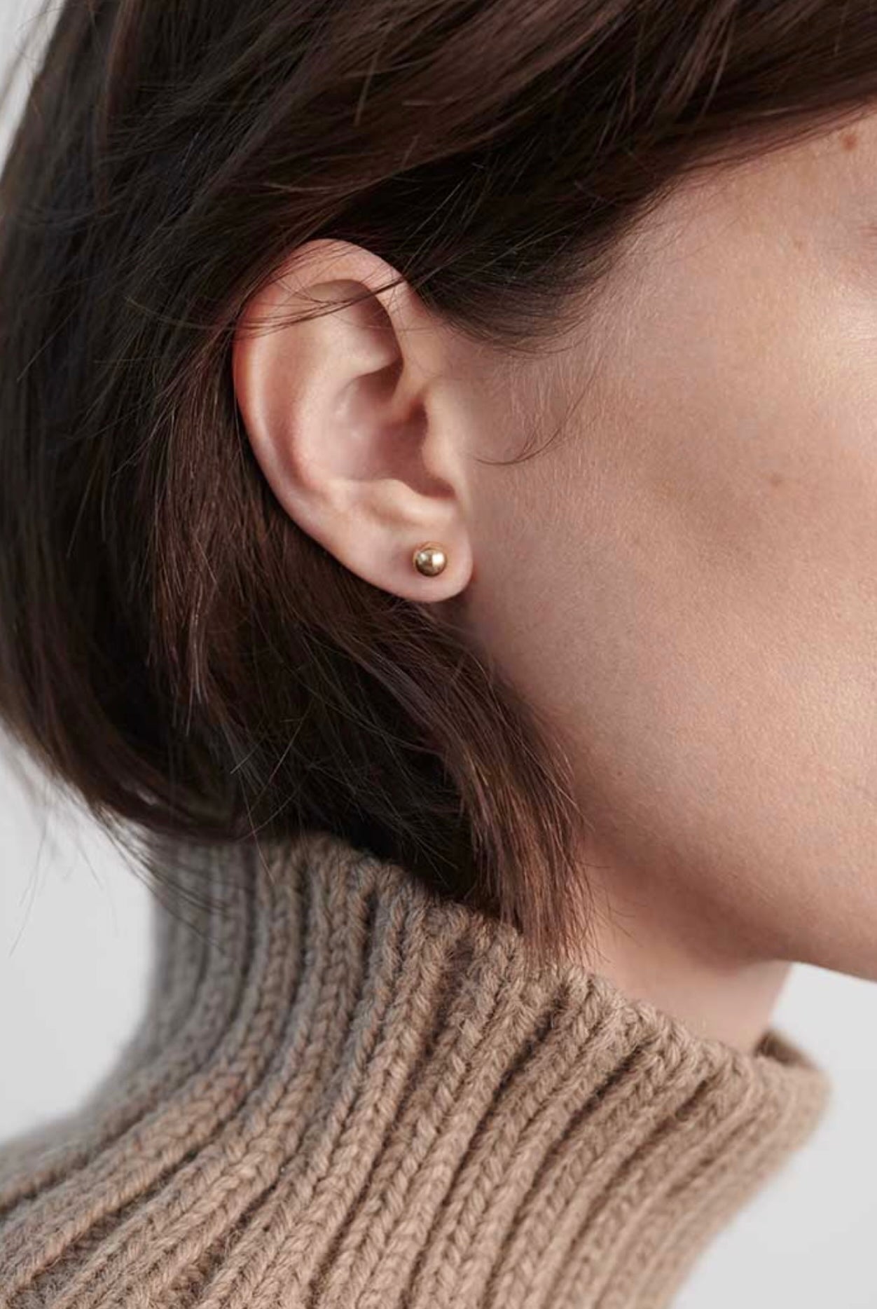 Model wearing small polished gold ball stud earrings with minimalist styling.