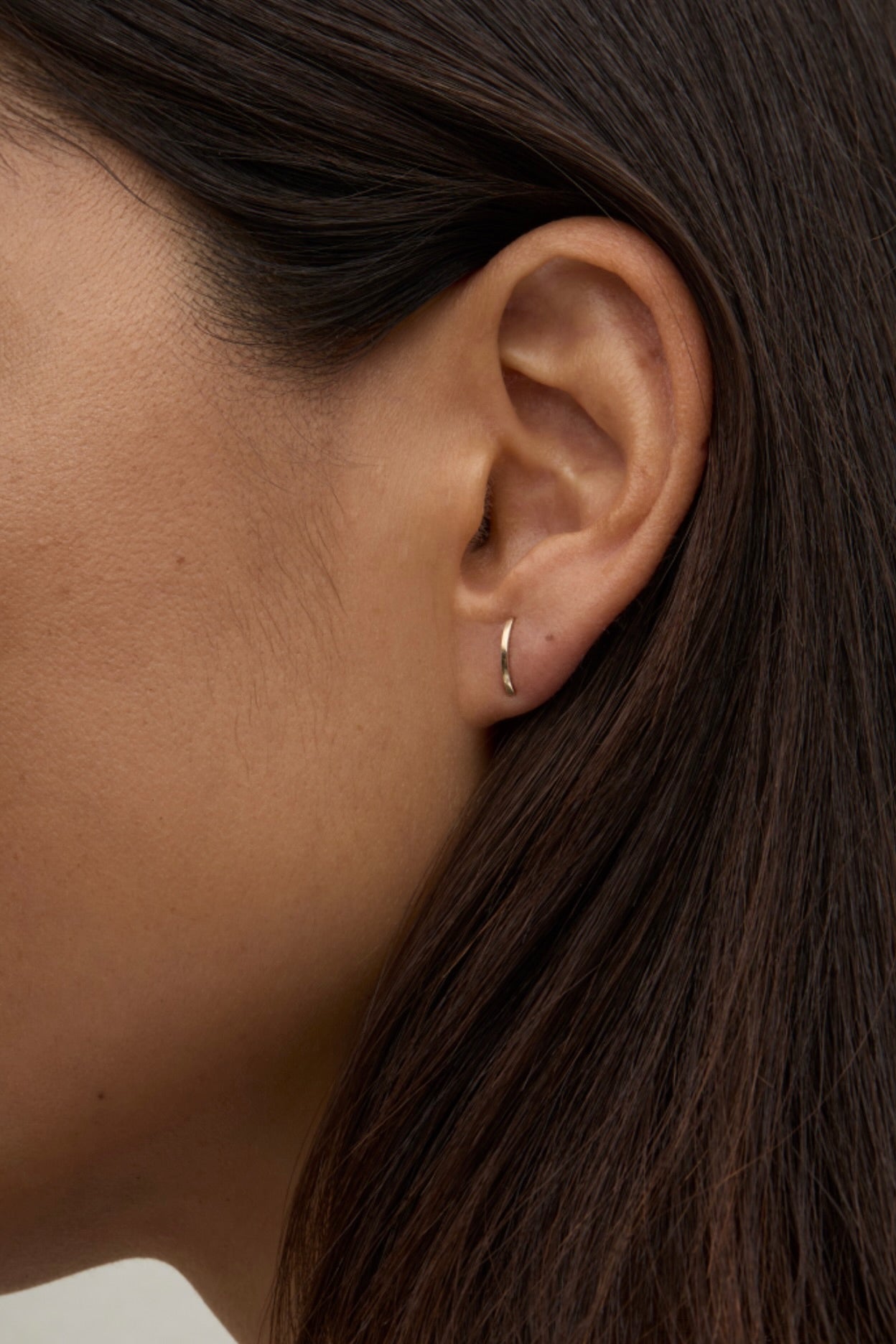Model wearing delicate 14K gold curved bar stud earring.