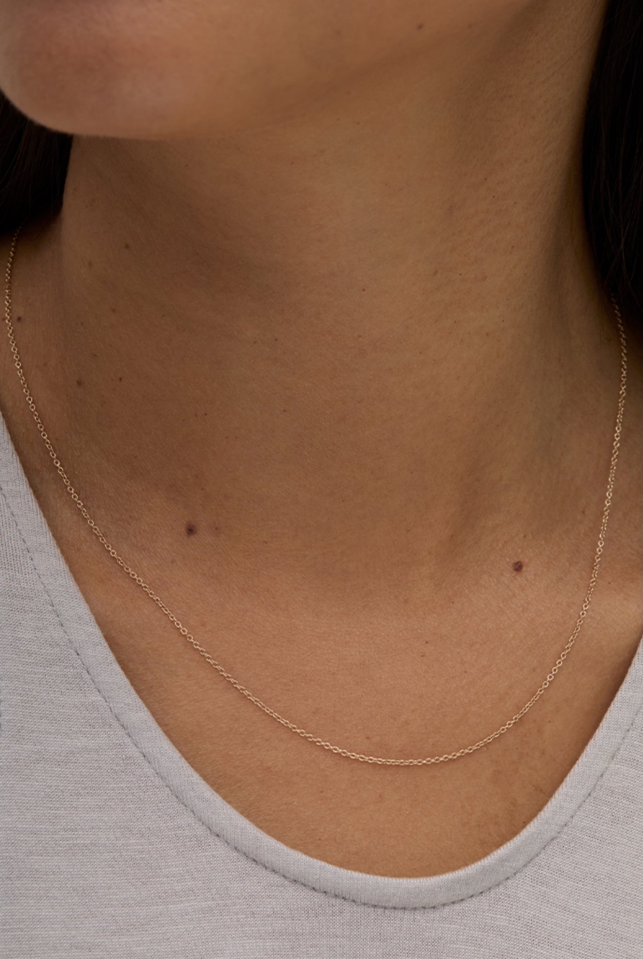 Model wearing minimalist 14k gold-filled layering necklace with grey top.