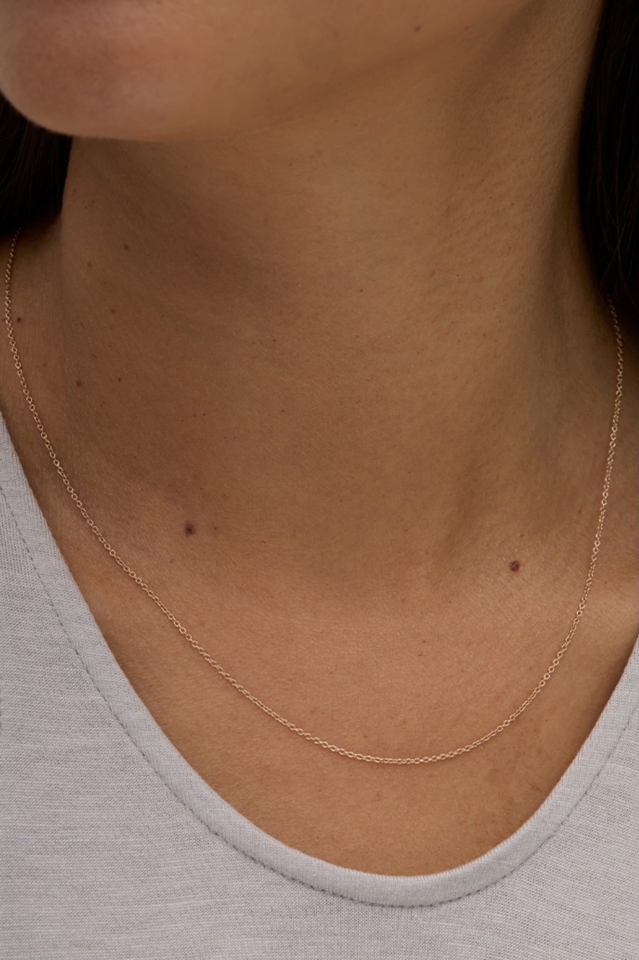 Model wearing minimalist 14k gold-filled layering necklace with grey top.