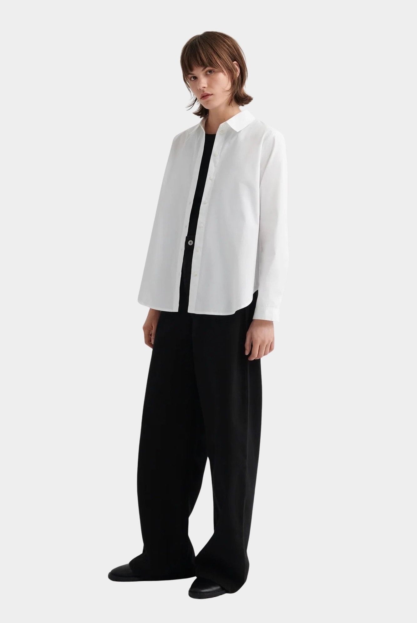 Kowtow Daily Shirt in white worn open over black top with wide leg trousers, full length view