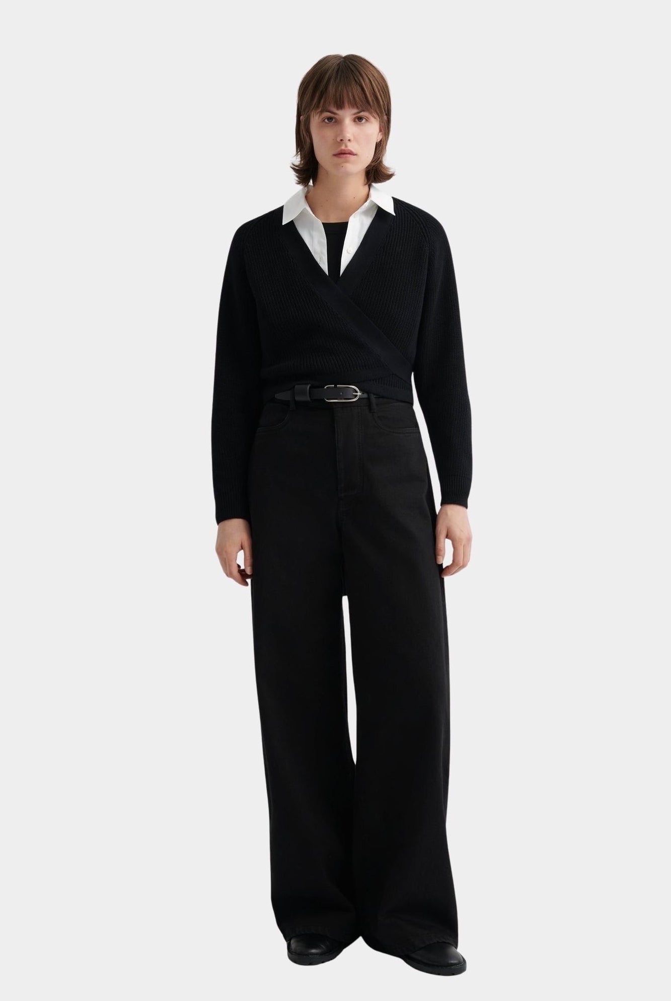 Kowtow Daily Shirt in white worn under black wrap sweater with wide leg trousers, full length view