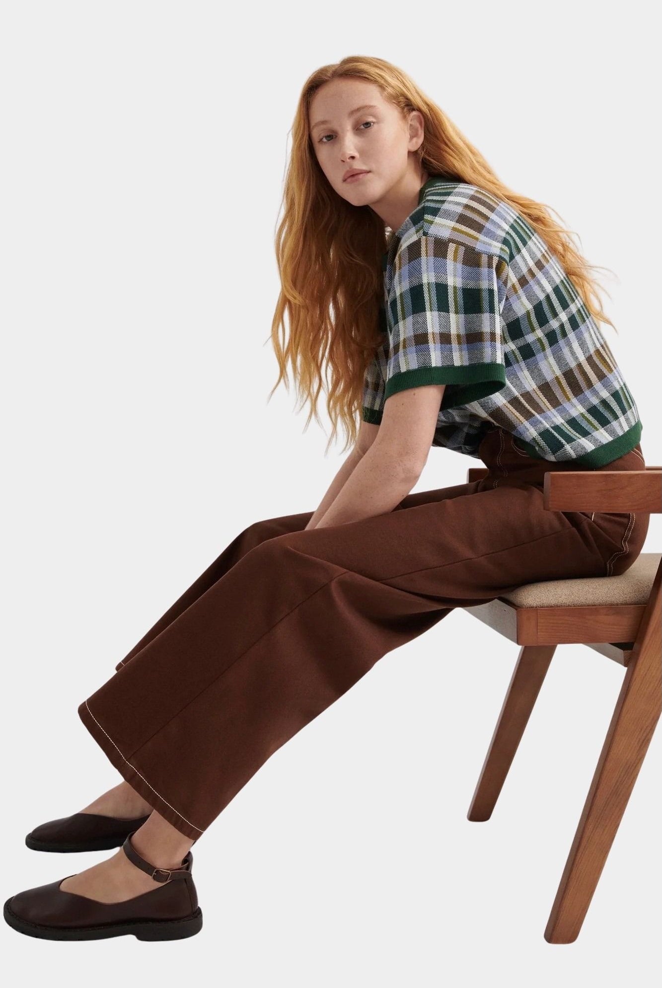 Kowtow Unity Jeans in brown denim worn with plaid knit top, seated side view