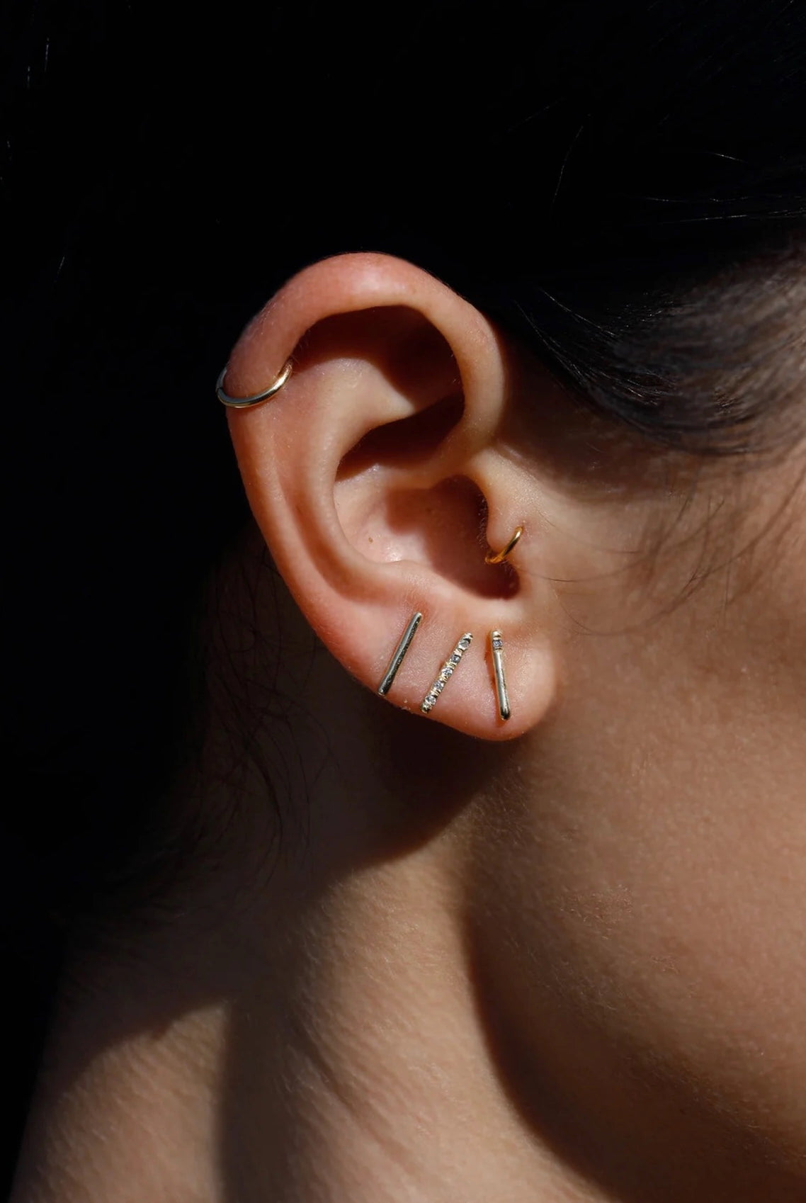 Model wearing 14K gold bar stud earrings in curated ear stack.