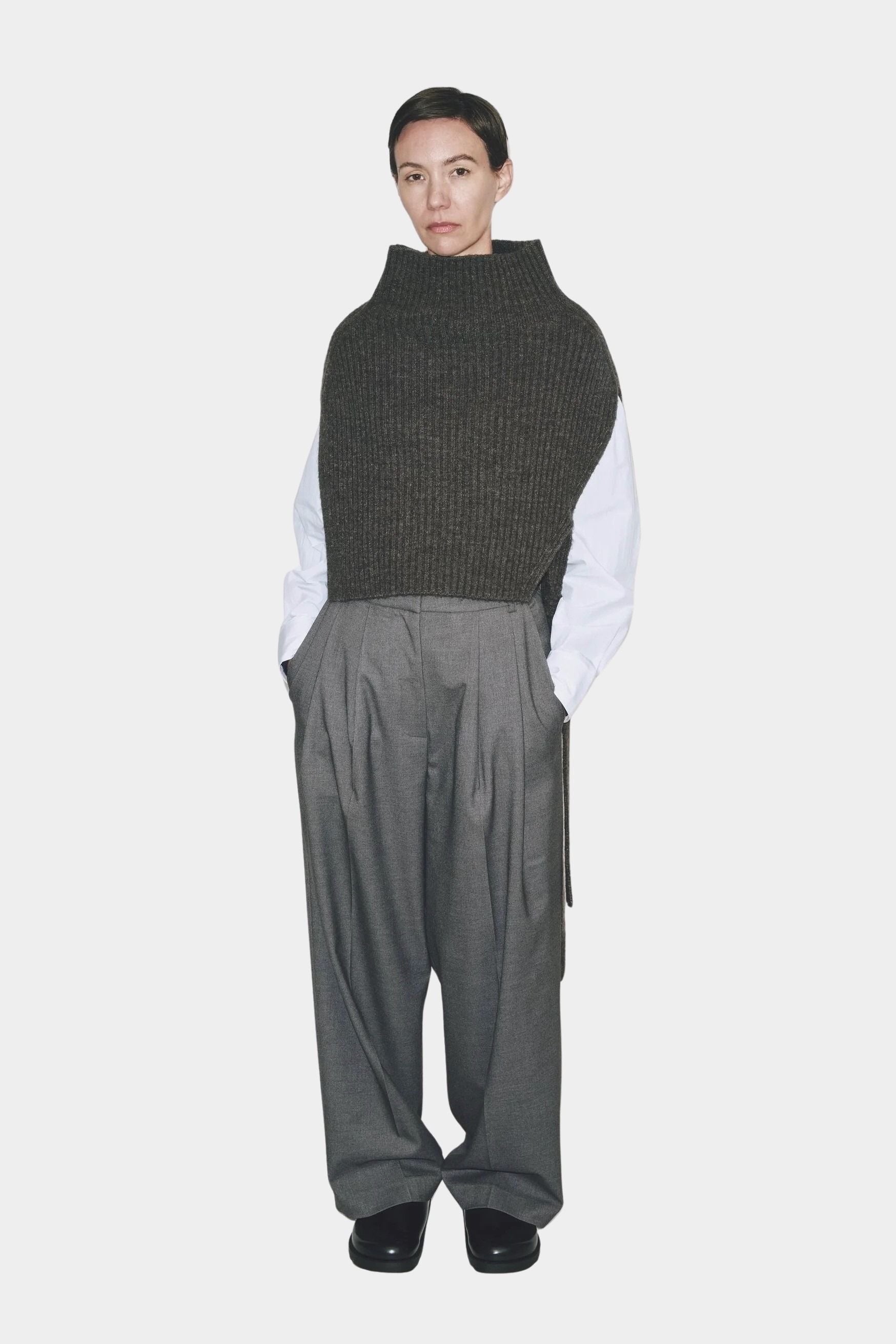 Model wearing charcoal ribbed knit neck warmer vest with high funnel neck and side ties