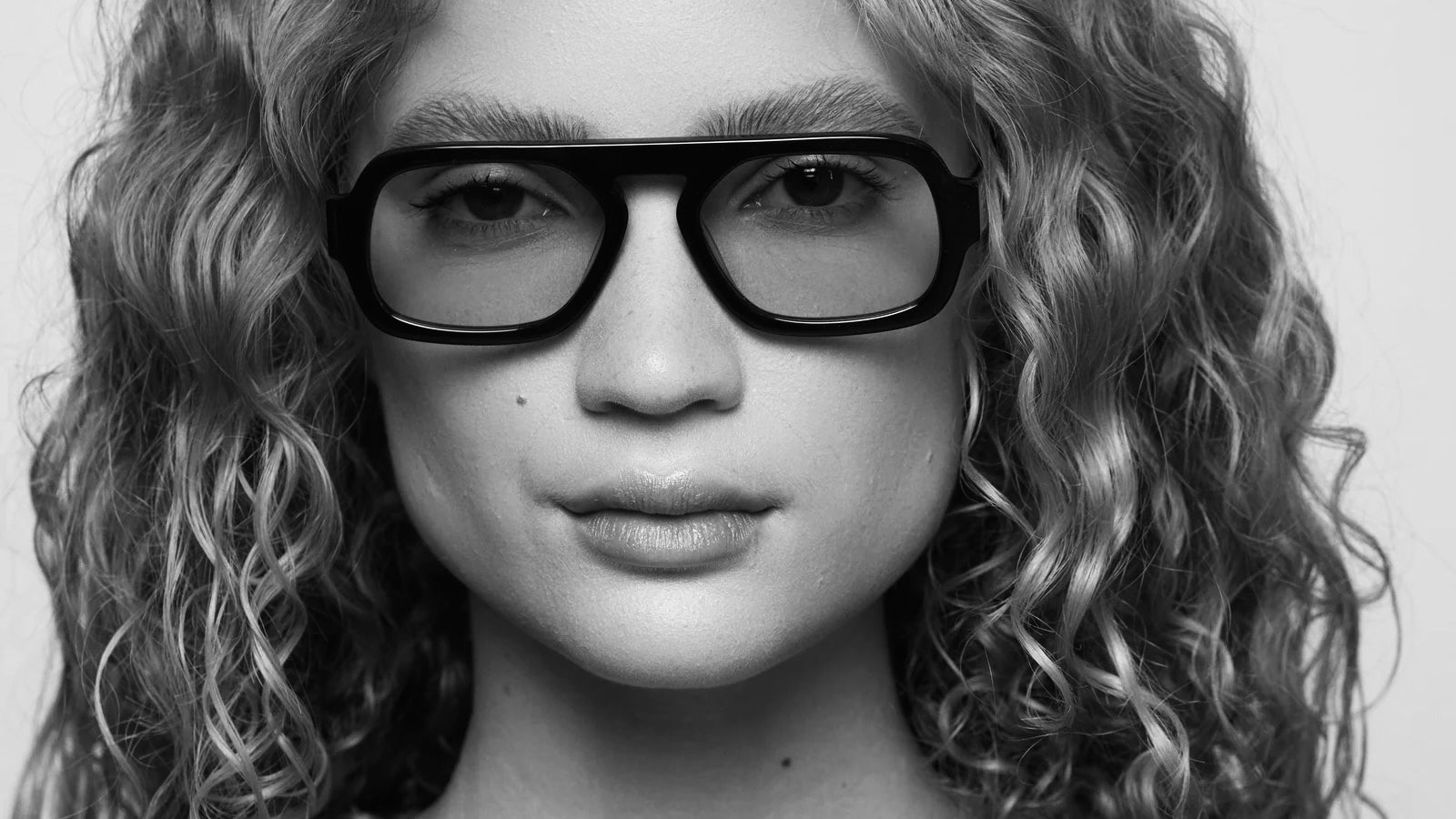 Black and white close-up portrait of model wearing oversized black Elisa Johnson sunglasses with sculptural square frames and a modern minimalist silhouette.