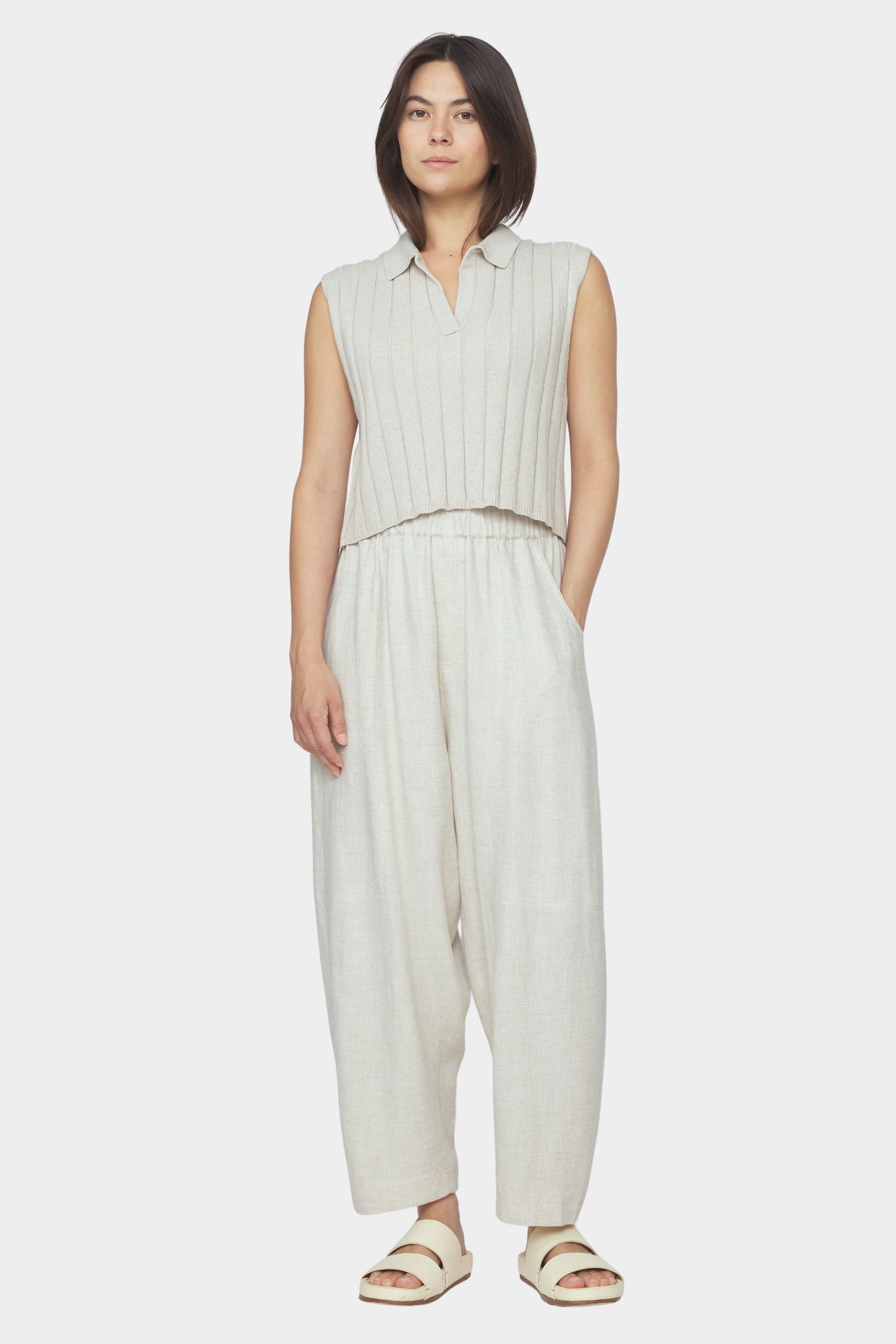 Front view of speckle beige collared knit vest with wide rib texture and cropped fit styled with relaxed light beige pants