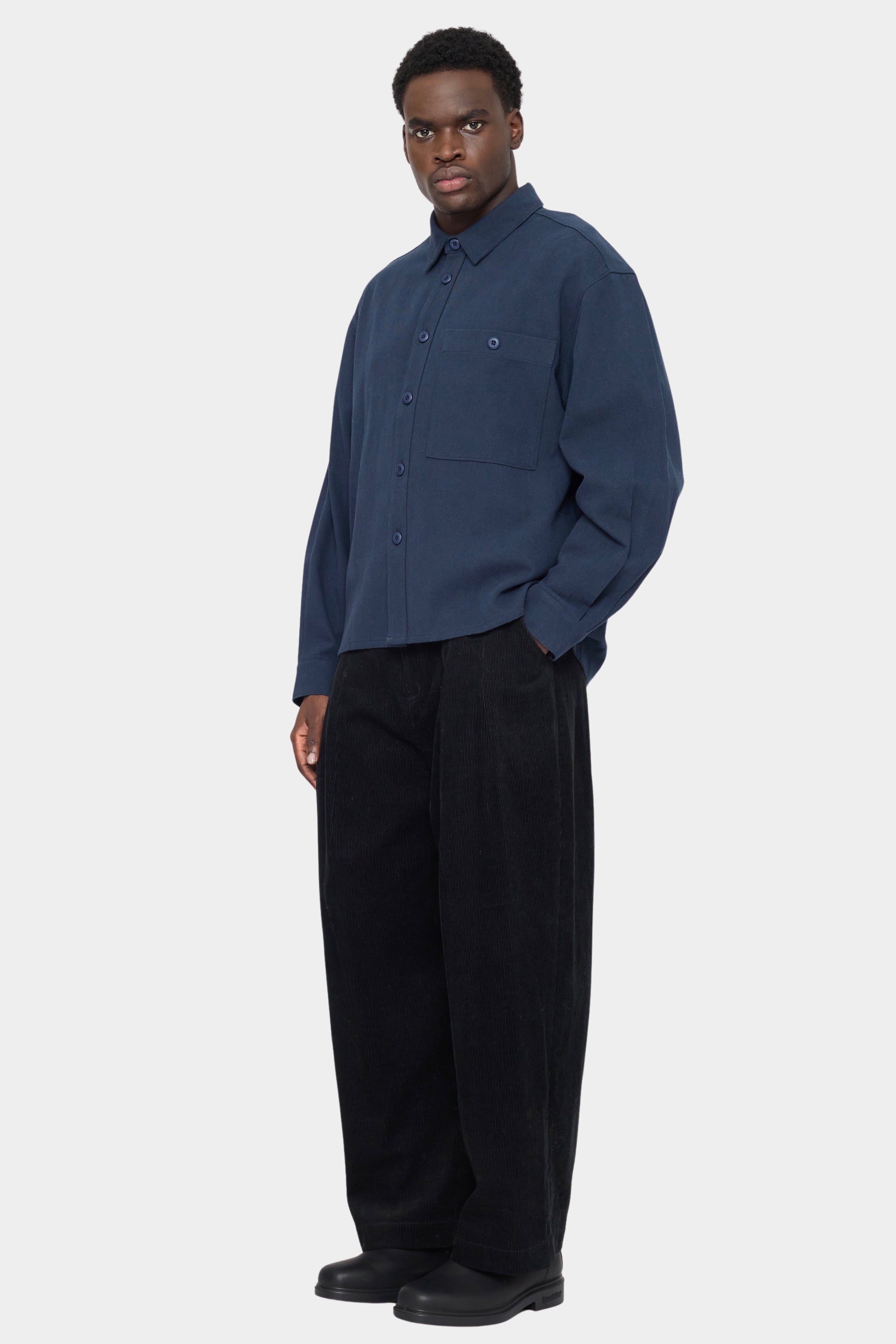 Angled front view of the navy Relaxed Pocket Shirt buttoned with black wide leg trousers