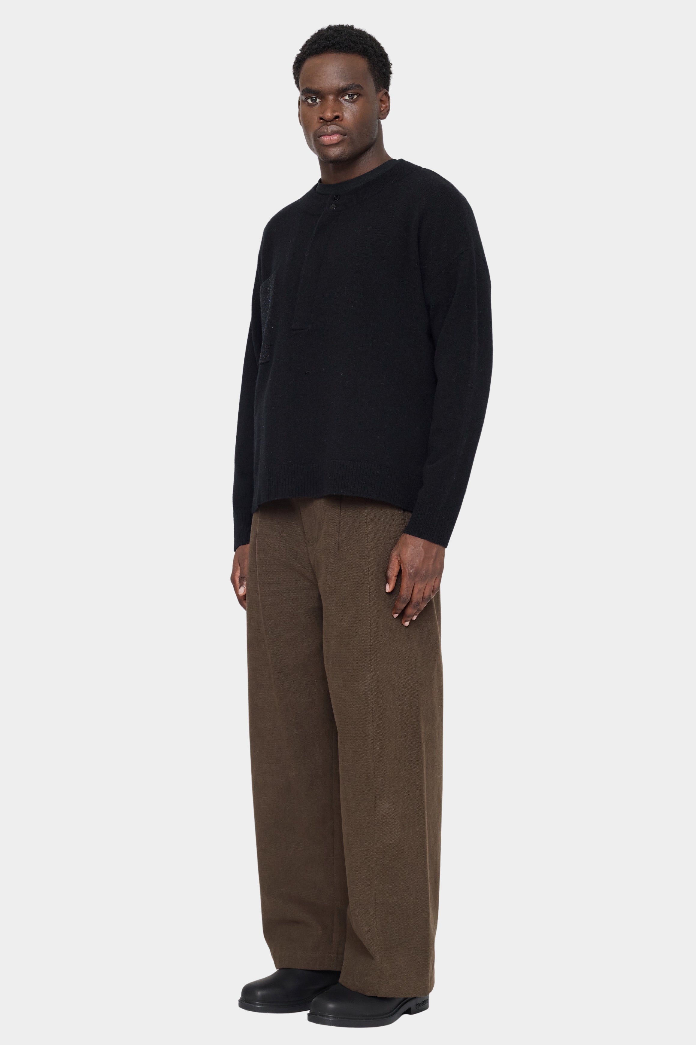 Angled front view of the black merino sweater showing its contrast patch pocket and button placket