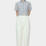 Front view of navy striped cropped button down shirt with short sleeves styled with ivory high waisted trousers