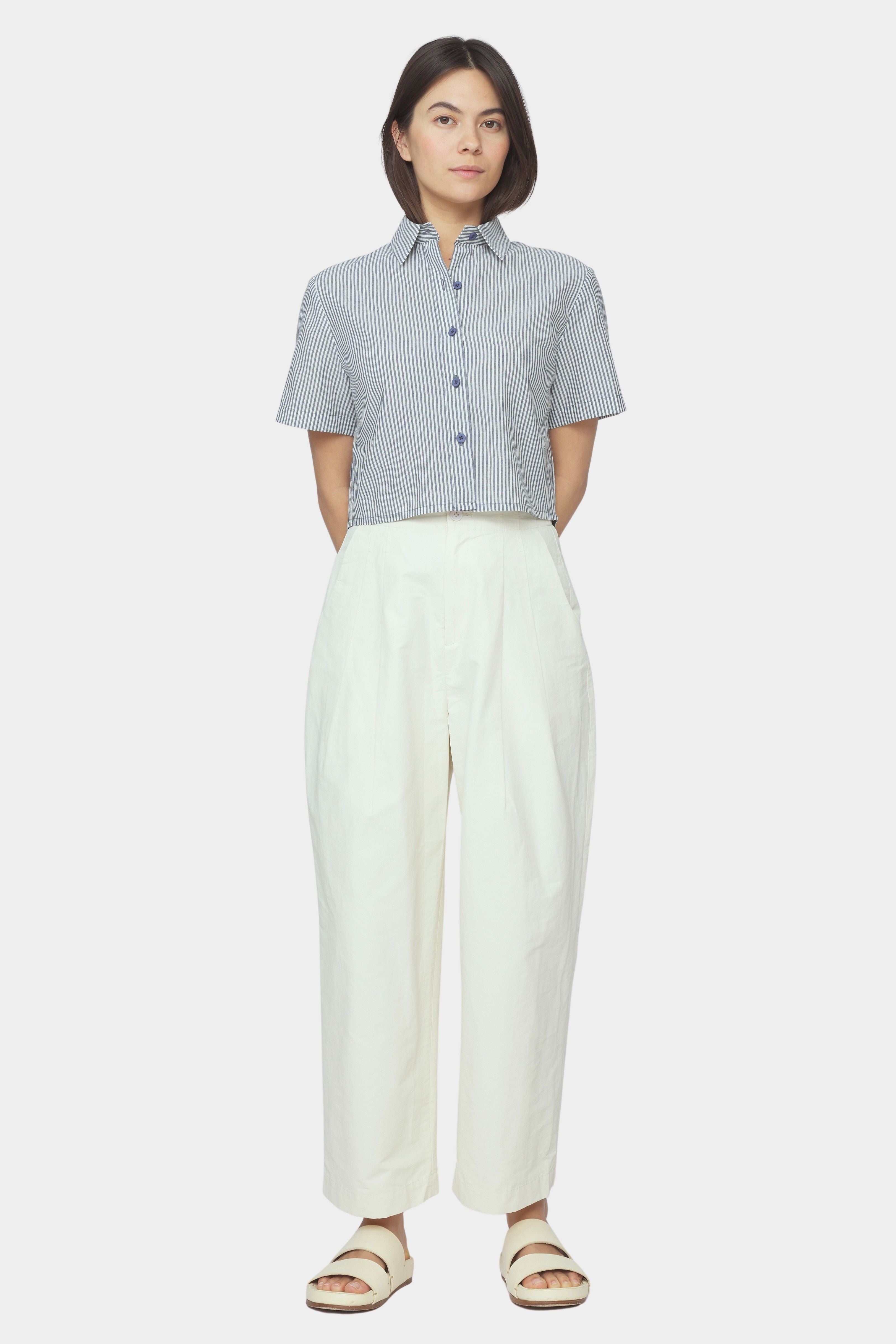 Front view of navy striped cropped button down shirt with short sleeves styled with ivory high waisted trousers