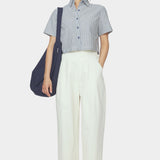 Front view of navy striped cropped shirt with short sleeves and button front styled with ivory trousers and a navy shoulder bag