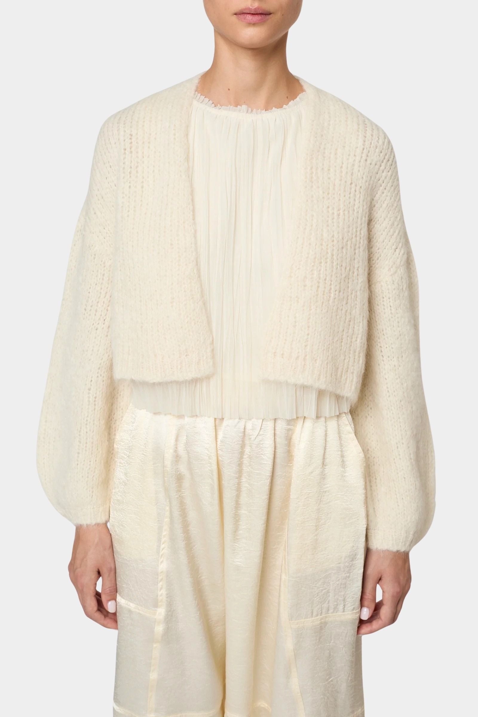 Atelier Delphine Super Crop Cora cardigan in cream front view worn over sheer top showing cropped silhouette and open front