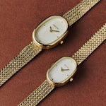 Two BREDA Jane Tethered gold watches in different sizes styled on a warm brown background