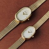 Two BREDA Jane Tethered gold watches in different sizes styled on a warm brown background