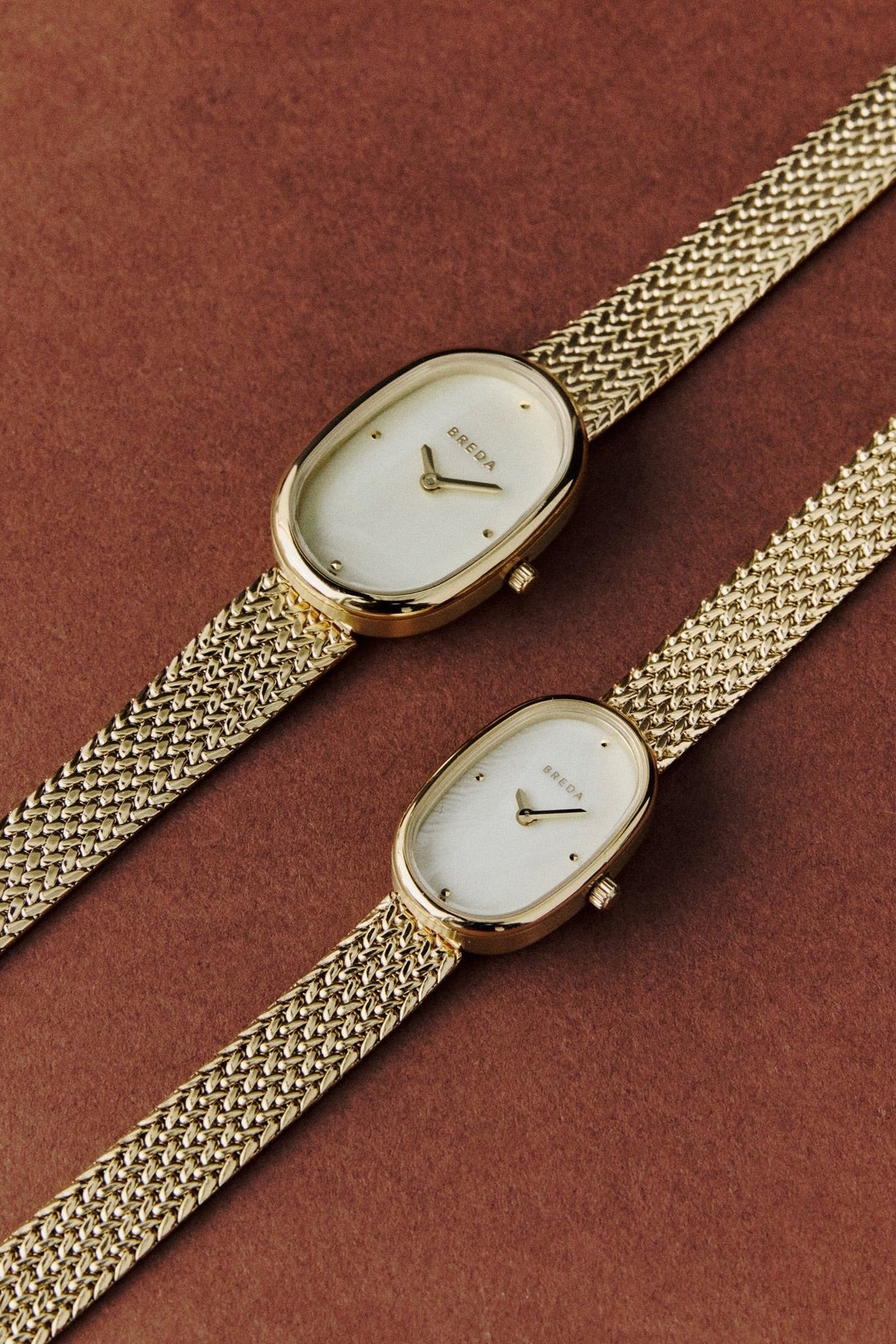 Two BREDA Jane Tethered gold watches in different sizes styled on a warm brown background