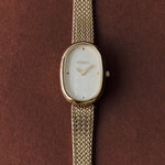 BREDA Jane Tethered 23mm gold watch with textured bracelet photographed against a rich brown background