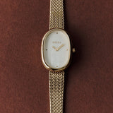 BREDA Jane Tethered 23mm gold watch with textured bracelet photographed against a rich brown background