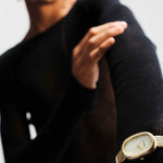 BREDA Jane Tethered gold watch styled over a black knit sleeve, showing its oval face and woven metal band