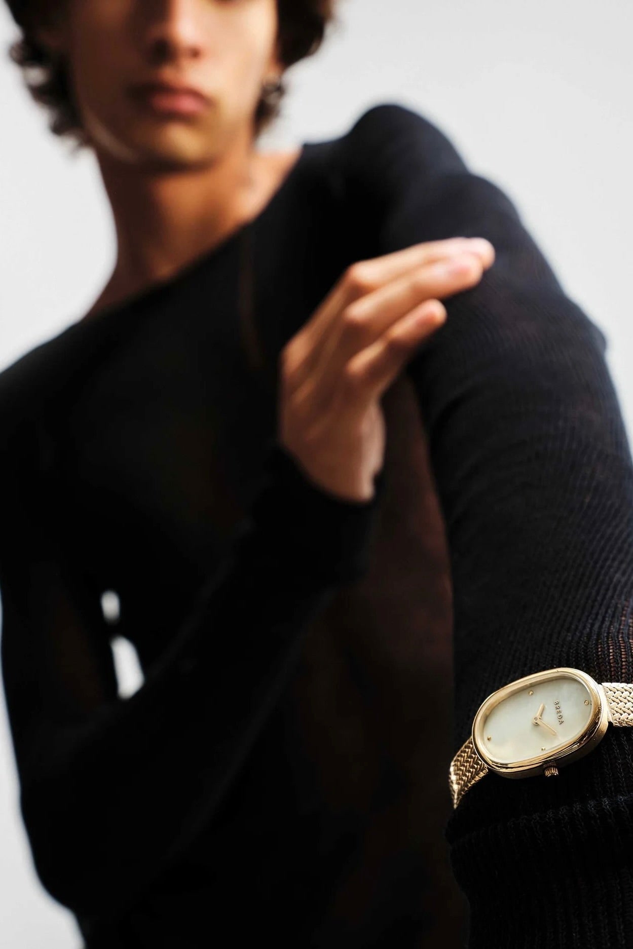 BREDA Jane Tethered gold watch styled over a black knit sleeve, showing its oval face and woven metal band
