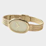 BREDA Jane Tethered gold watch with curved woven bracelet and visible clasp on a light gray background