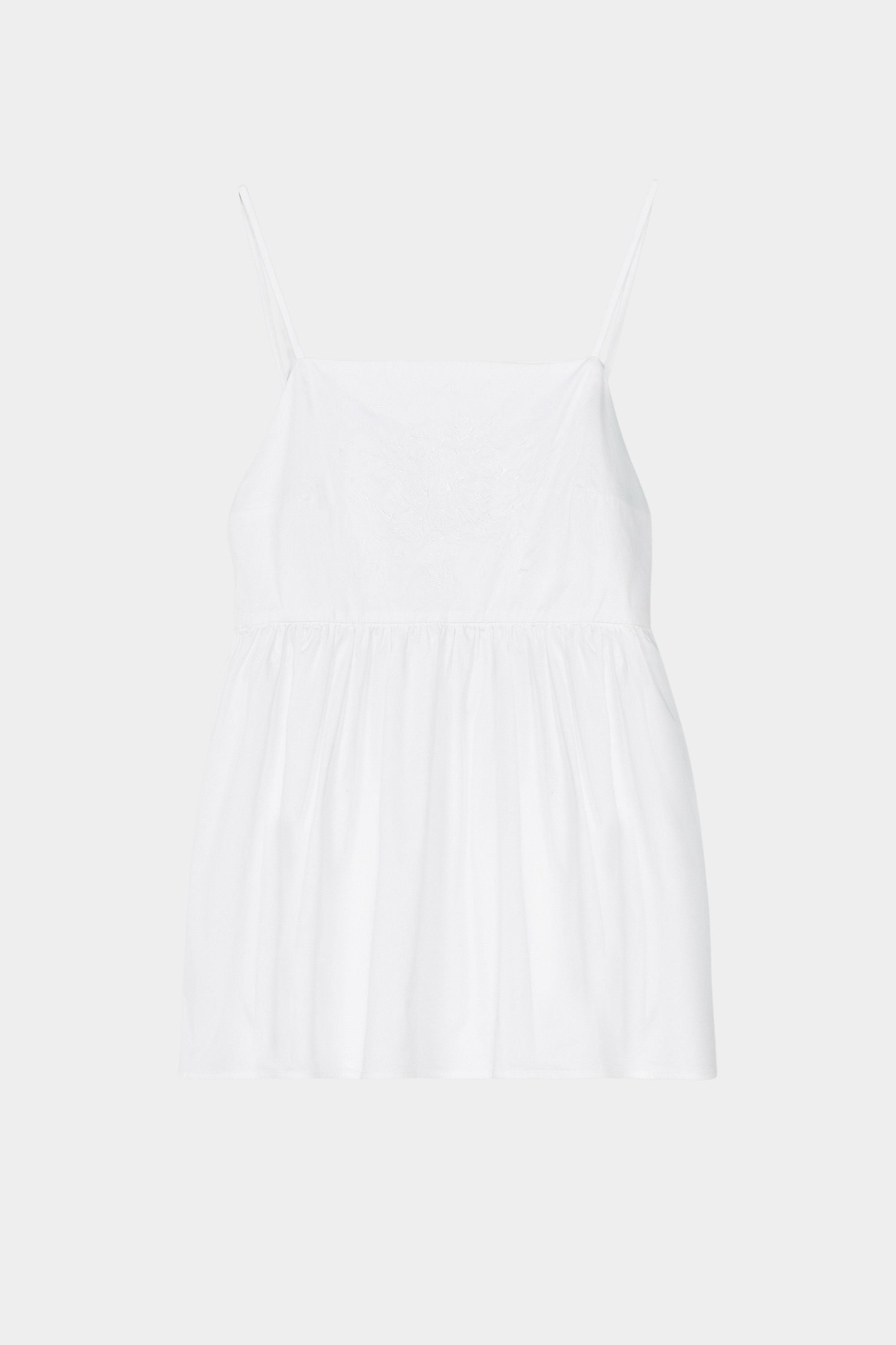 White cotton camisole top with tonal embroidery, thin straps, and gathered waist seam
