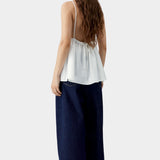 White camisole top with thin straps, gathered back with tie detail, and soft drape