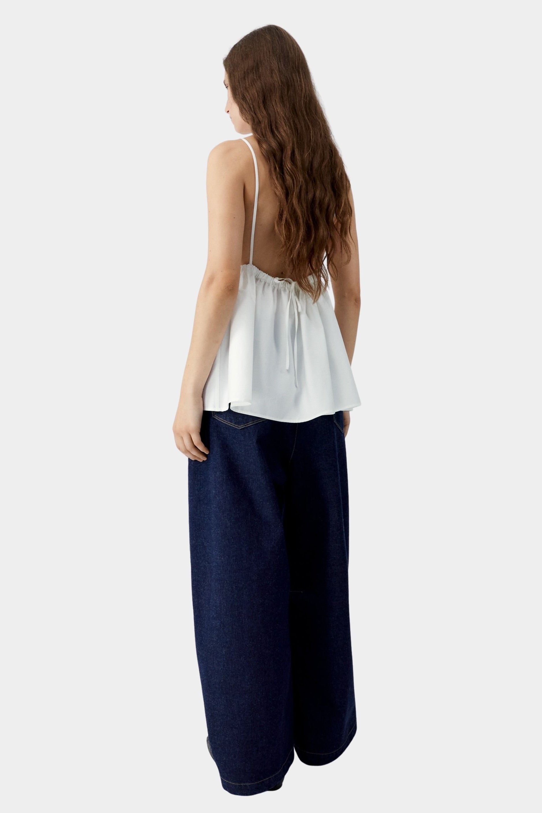 White camisole top with thin straps, gathered back with tie detail, and soft drape