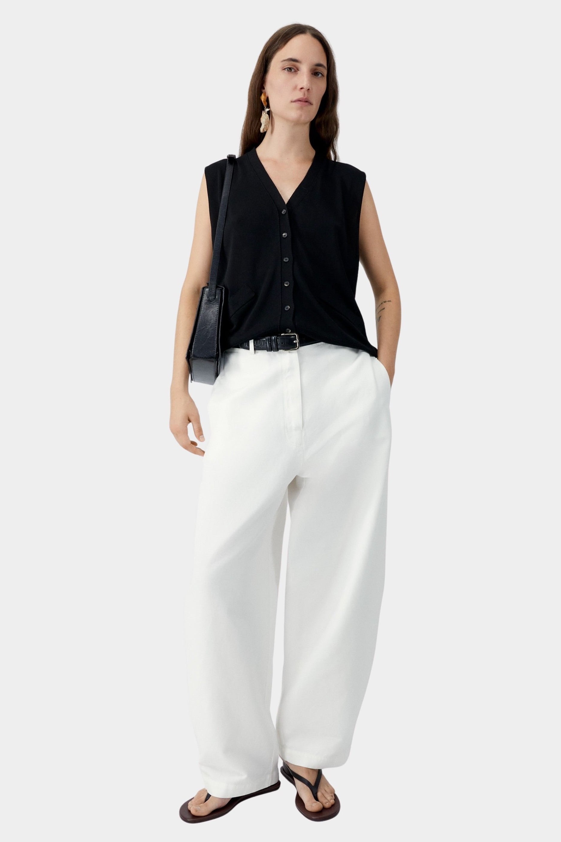 White cotton linen curved pants with relaxed fit and subtle taper, worn with black sleeveless top and sandals
