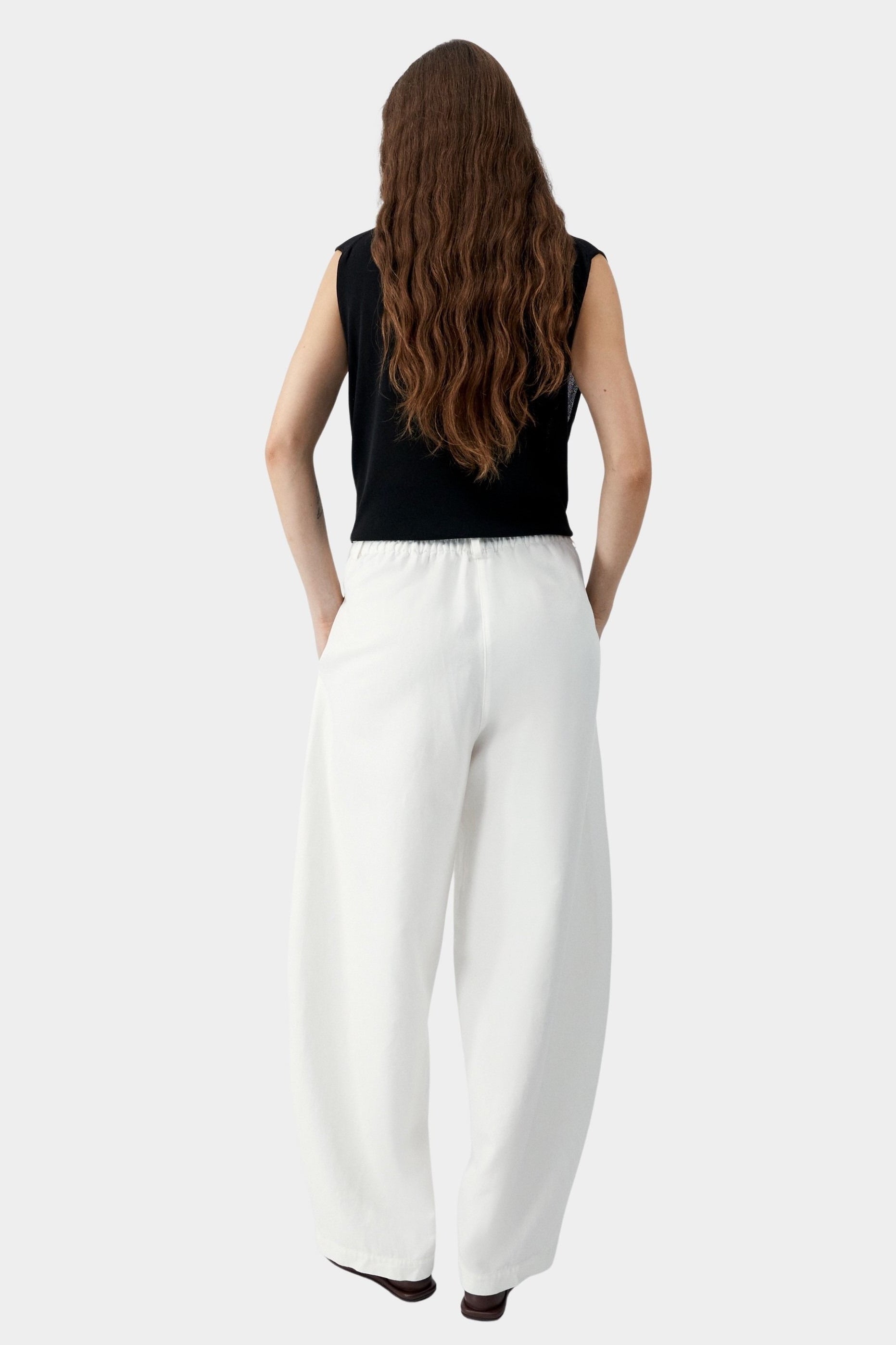 White cotton linen curved leg pants with elastic waistband and relaxed tapered silhouette, back view