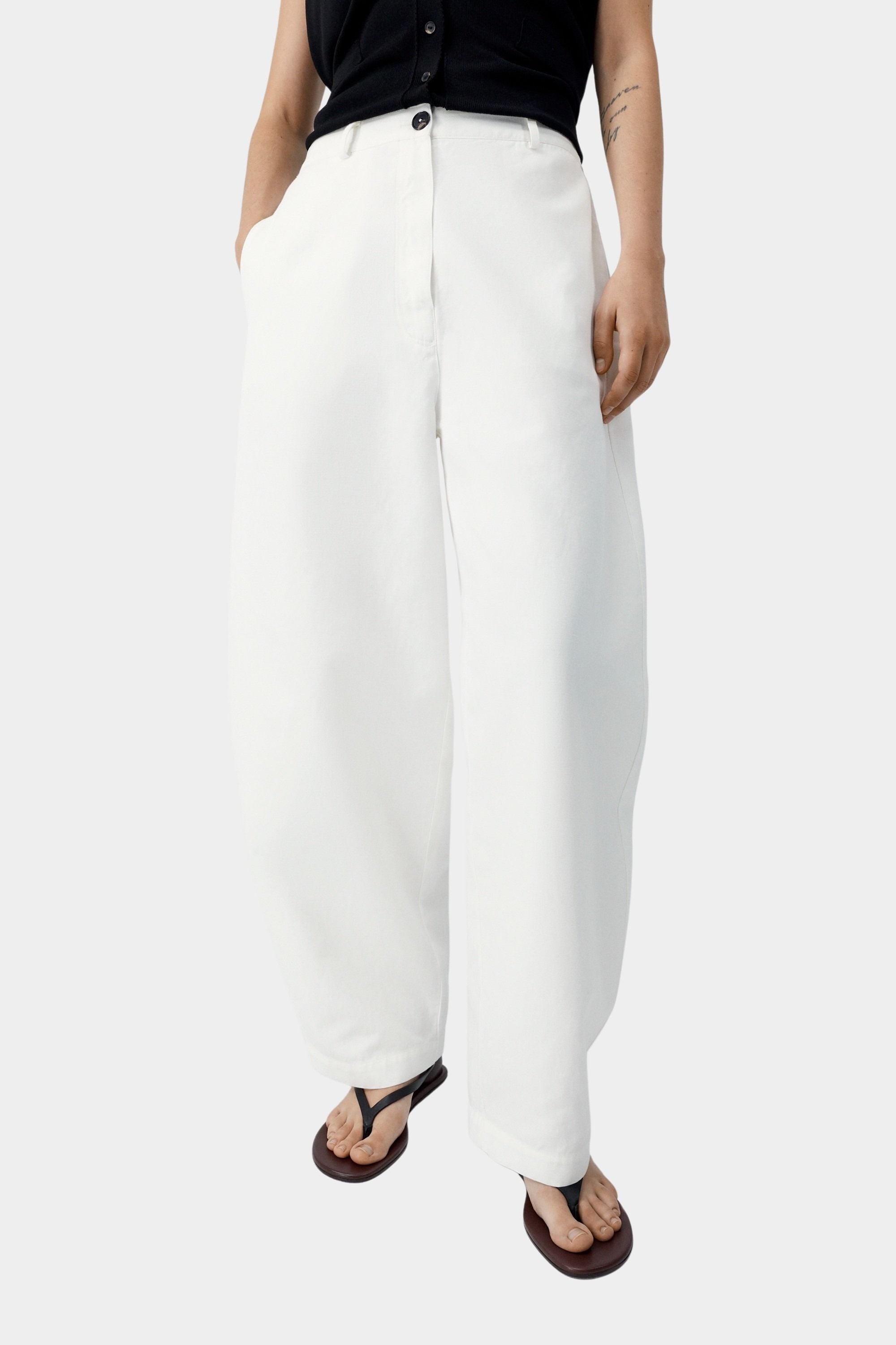 White cotton linen pants with curved leg shape, front button closure, and relaxed tailored fit