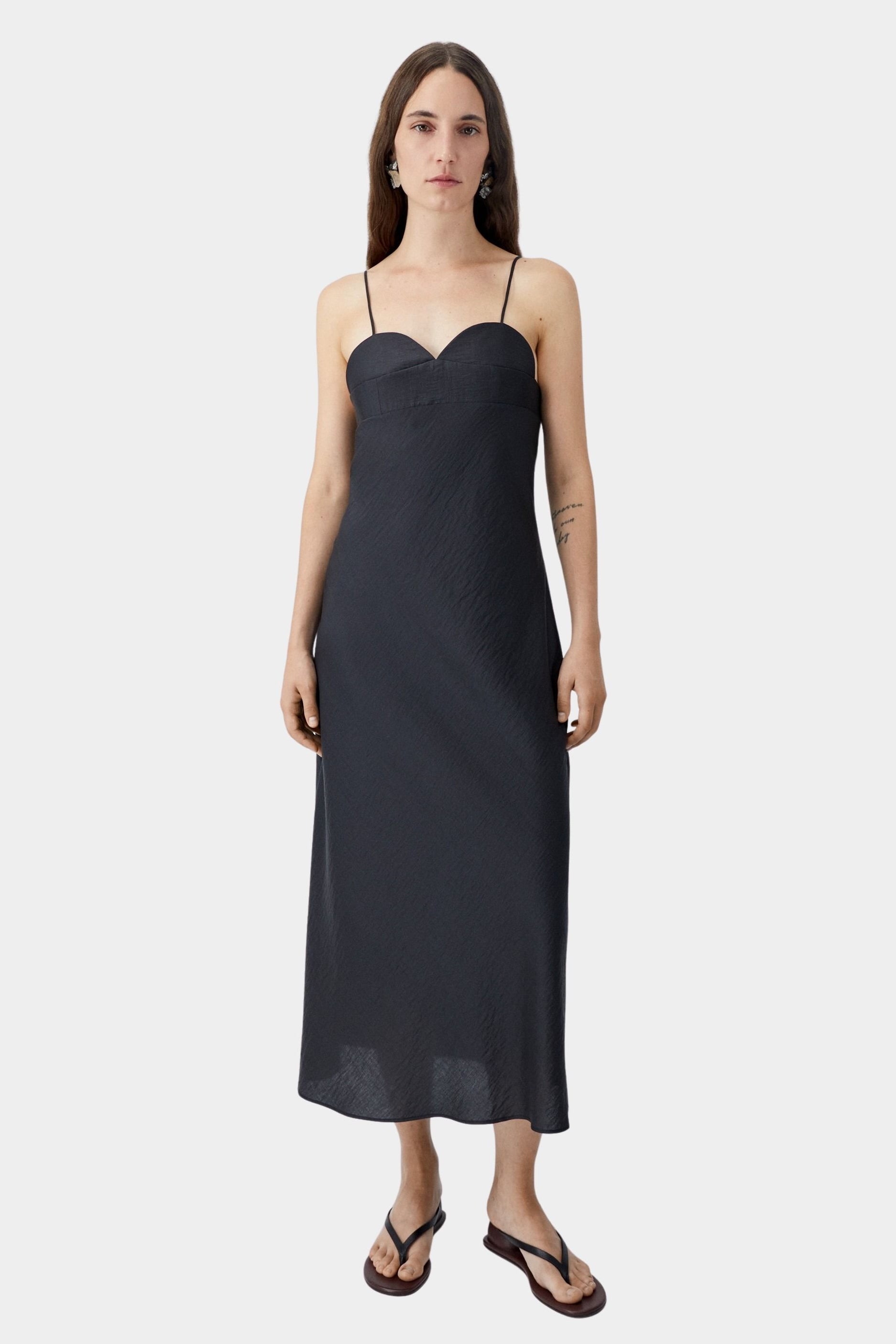 Black midi dress with heart-shaped neckline and slim straps, worn with flat sandals and fluid silhouette