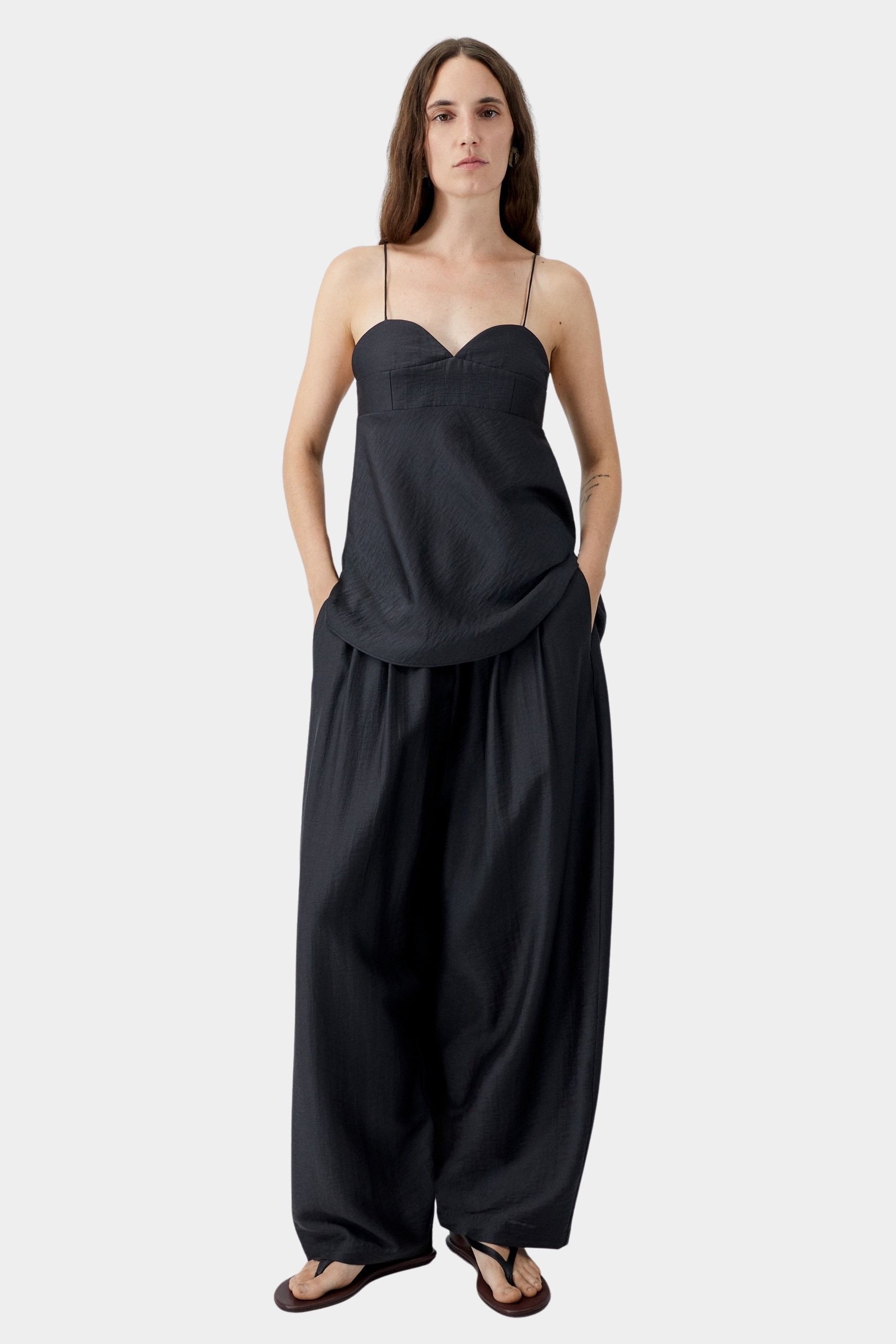 Black wide leg maxi pants with elastic waist and fluid drape, worn with black camisole and sand