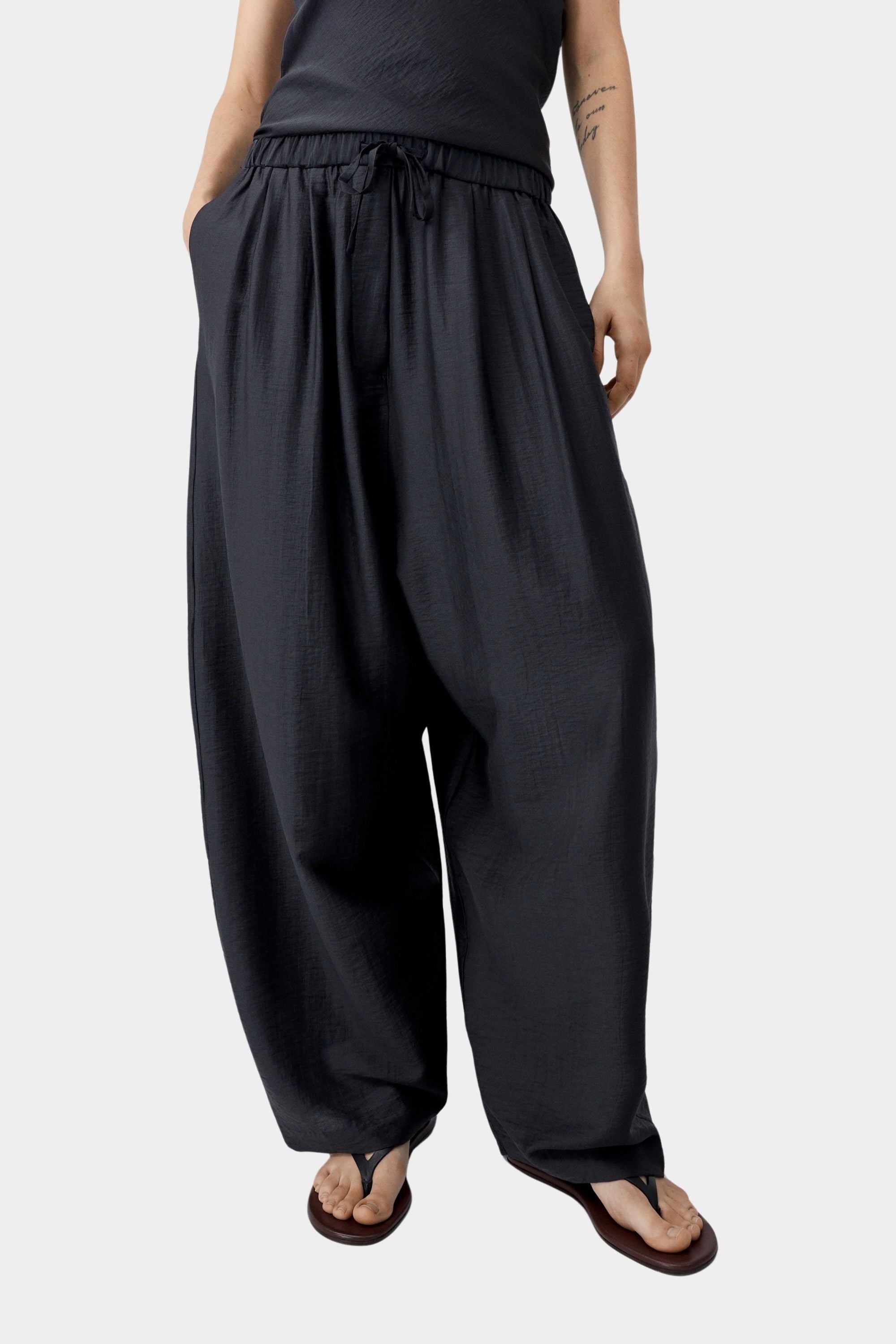 Black wide leg pants with elastic waist and drawstring detail, showing soft volume and drape