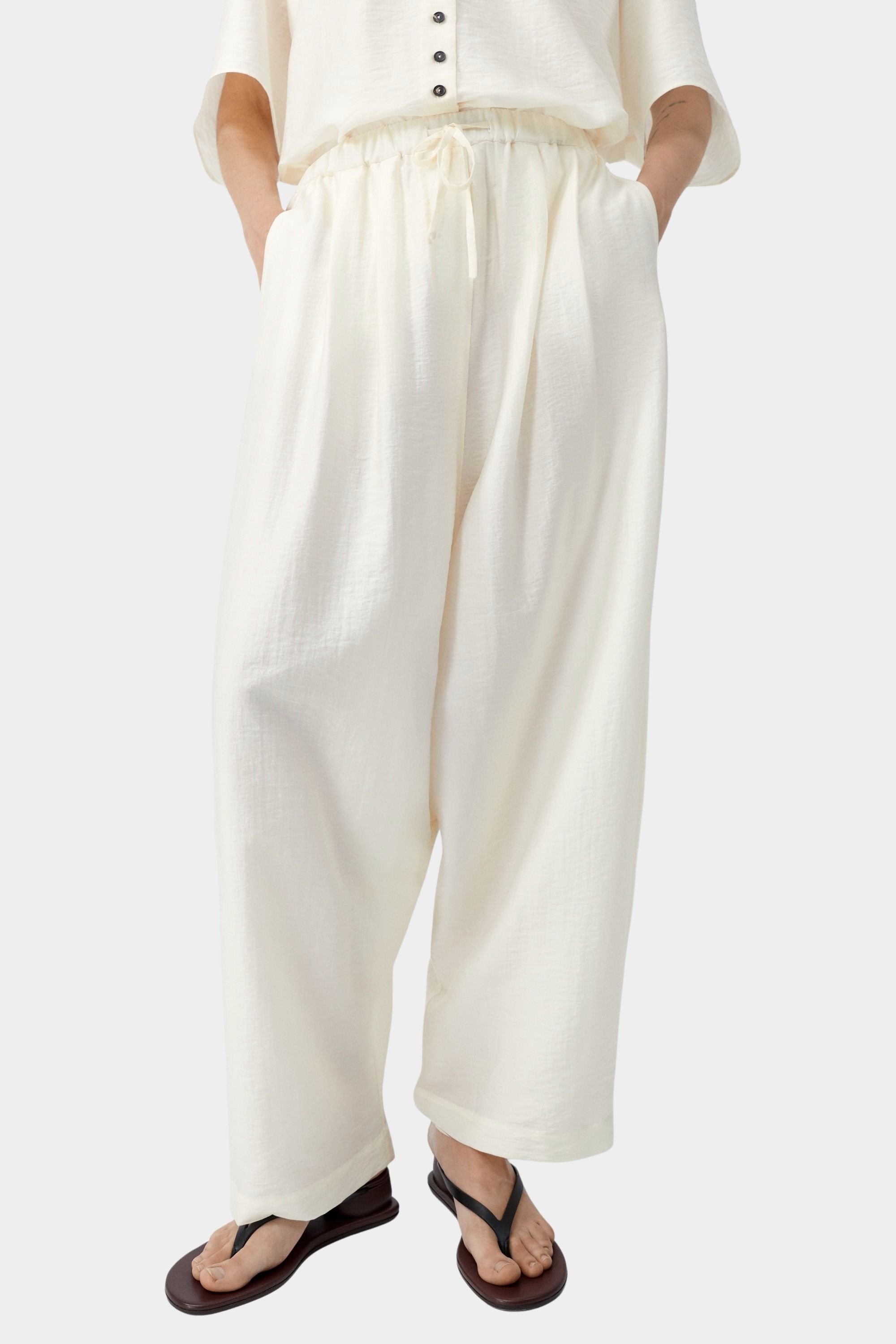 Cream wide leg pants with elastic waist and drawstring detail, highlighting soft texture and volume