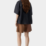 Black short sleeve shirt with relaxed oversized fit and clean back drape, worn with brown tailored shorts and sandals