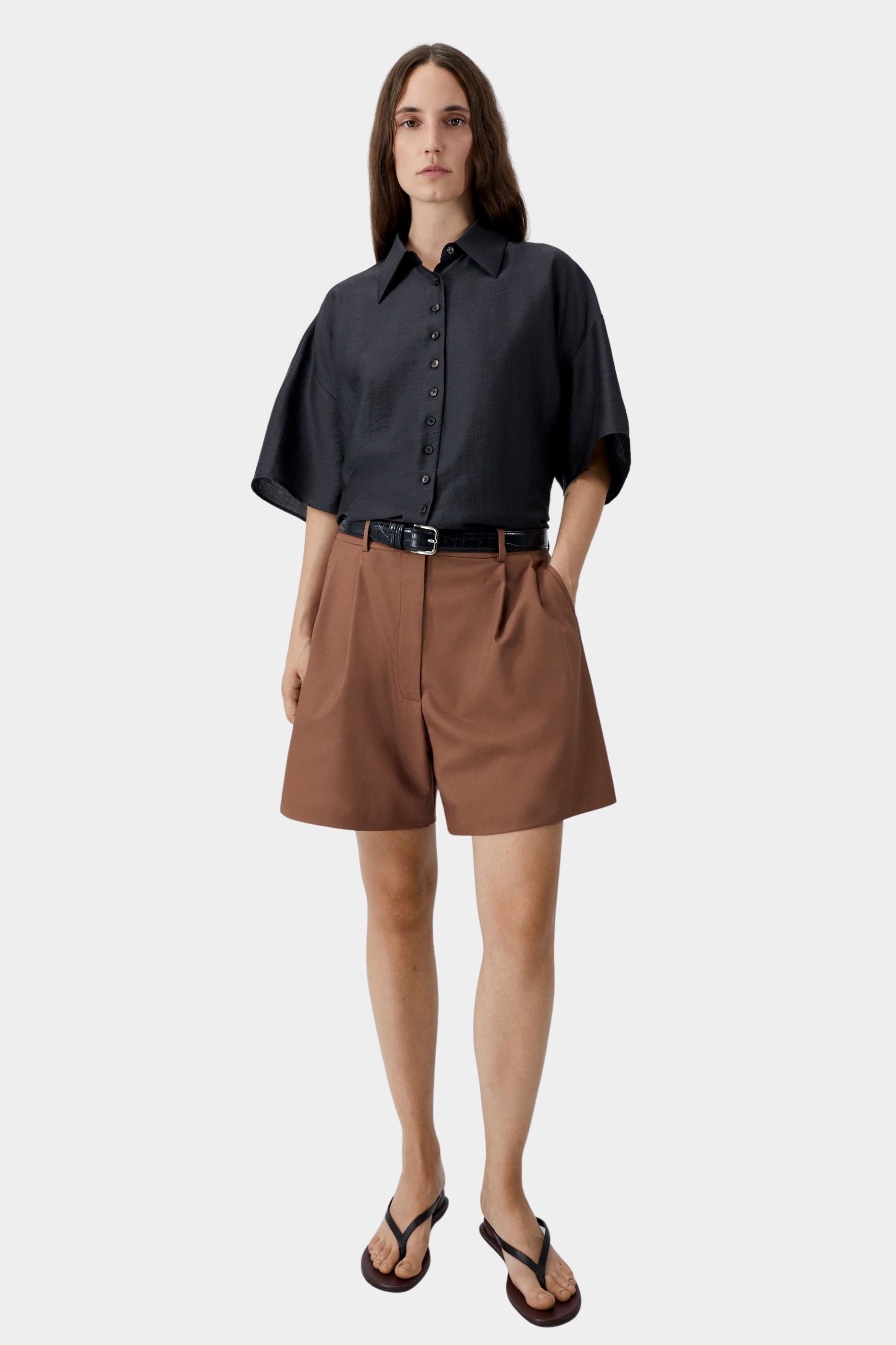 Black short sleeve shirt with button front and oversized fit, worn with brown tailored shorts and sandals