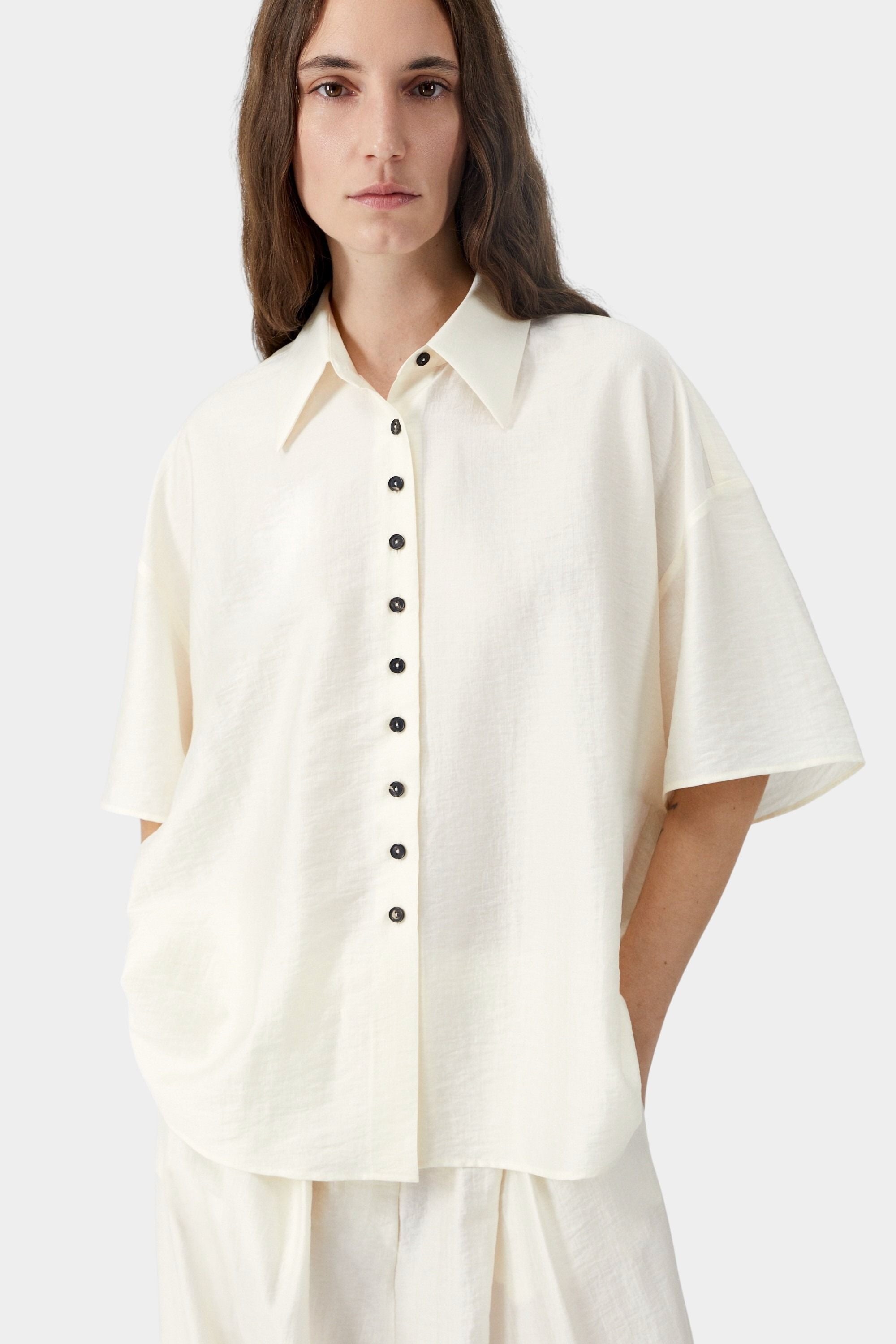 Cream short sleeve blouse with button closure, pointed collar, and soft airy texture detail