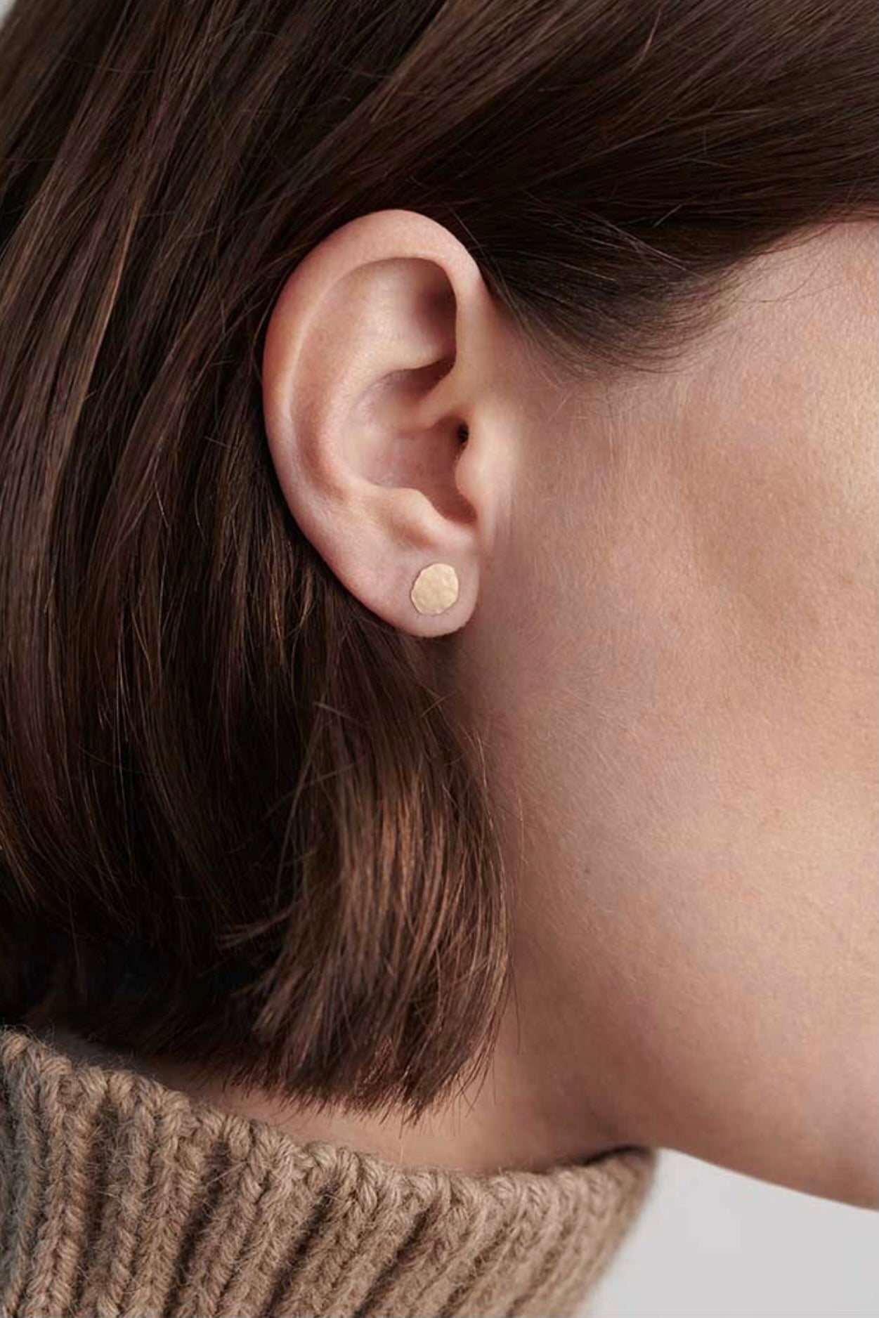 Model wearing small gold disc stud earrings with textured organic finish.