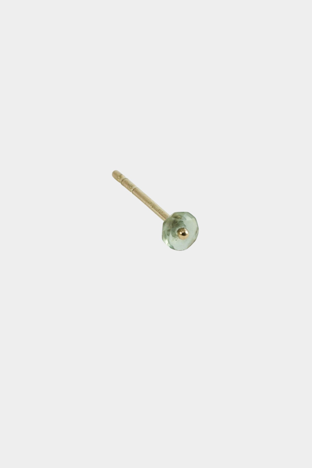 Close-up of gold stud earring with green gemstone detail on neutral background.