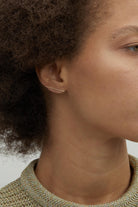 Model wearing 14K gold minimalist bar stud earrings.