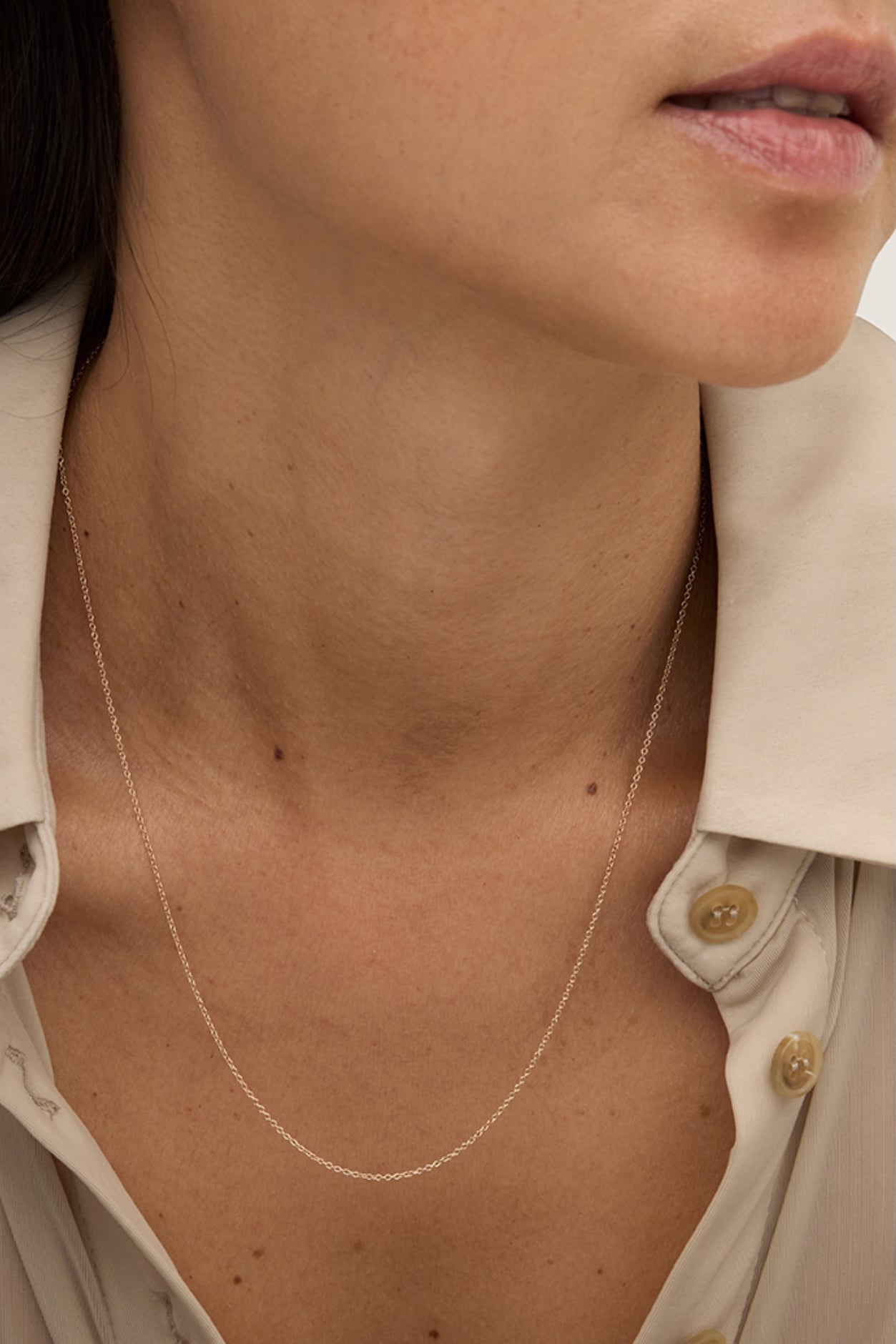 Model wearing delicate 14k gold-filled layering chain necklace with open collar shirt.