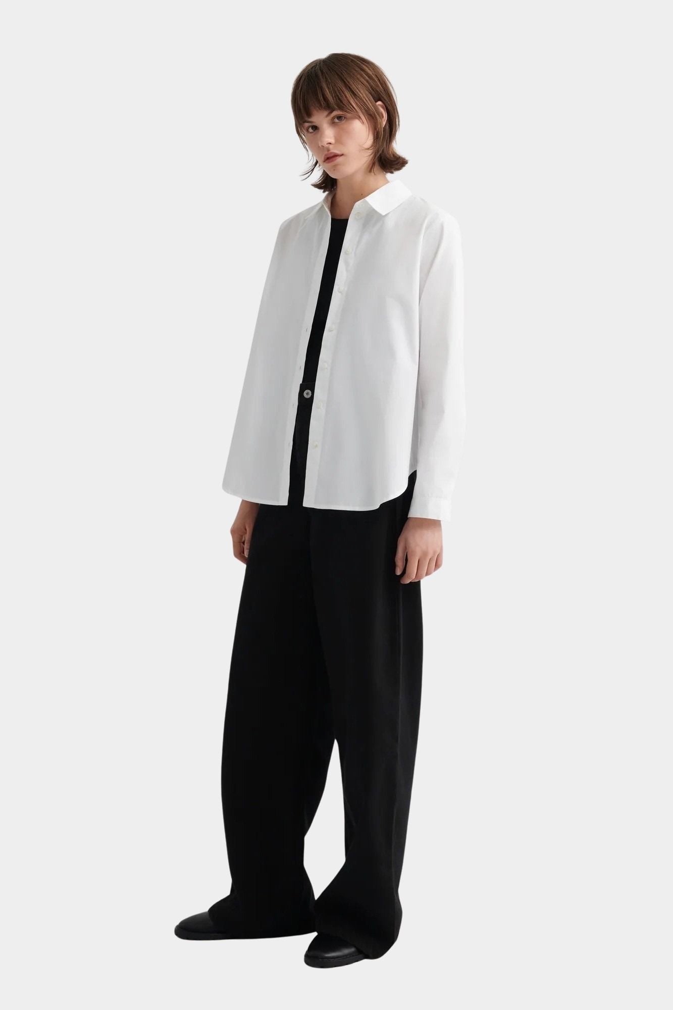 Kowtow Daily Shirt in white worn open over black top with wide leg trousers, full length view
