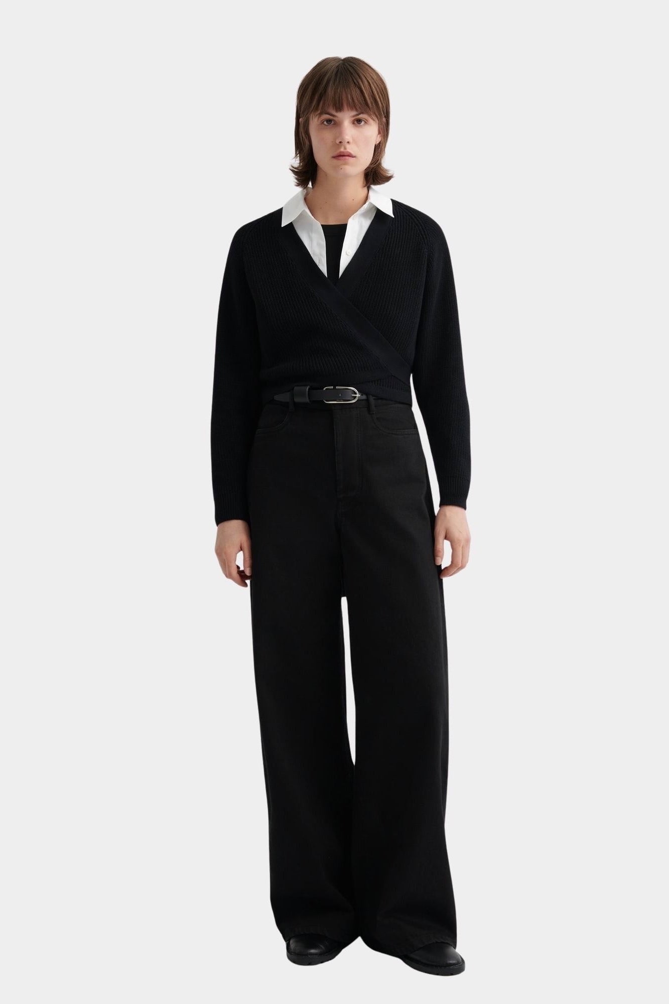 Kowtow Daily Shirt in white worn under black wrap sweater with wide leg trousers, full length view