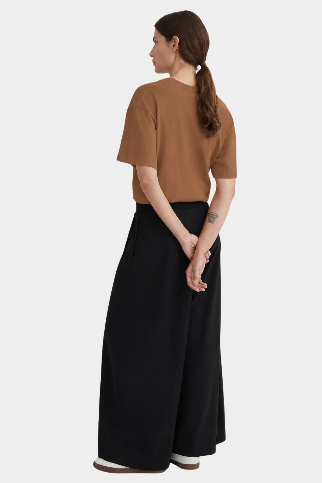 Back view of the black Kowtow Drape Pant worn with a brown tee and white sneakers at YUCCA Denver.