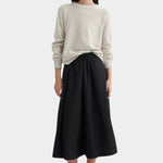 Full-length view of model wearing cream knit sweater styled with a black midi skirt and black lace-up shoes.