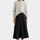 Full-length view of model wearing cream knit sweater styled with a black midi skirt and black lace-up shoes.