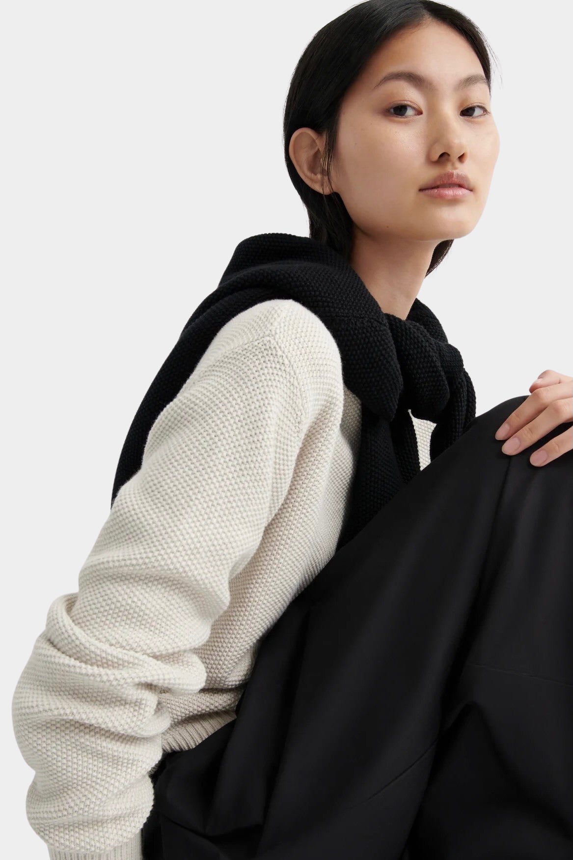 Close-up of model wearing a cream waffle-knit crewneck sweater with a black sweater draped over shoulders.