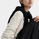 Close-up of model wearing a cream waffle-knit crewneck sweater with a black sweater draped over shoulders.